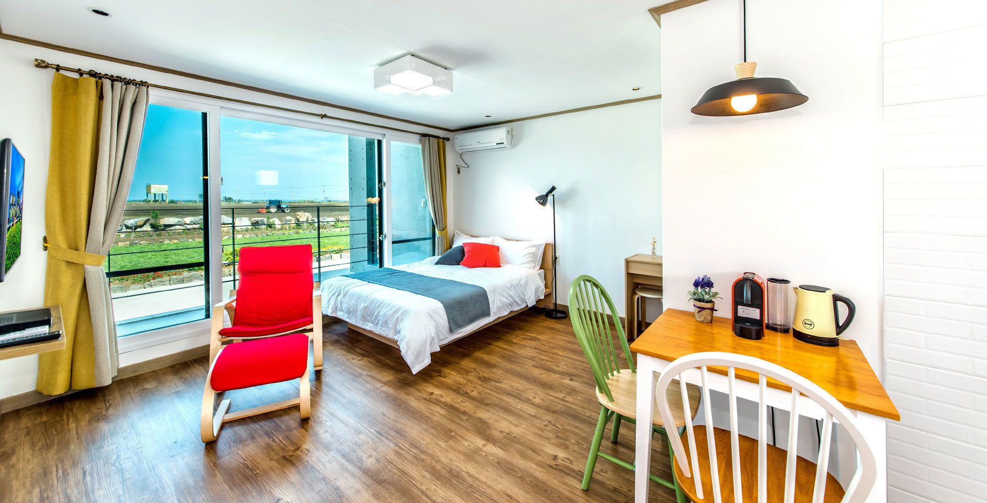 Habitación de hotel moderna con cama, escritorio con hervidor, una silla y vista a un paisaje a través de amplias ventanas.