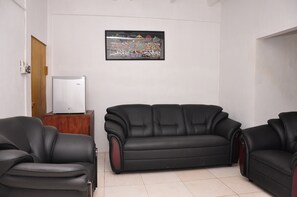 Una sala de estar con un sofá de cuero negro, un aparador de madera y una obra de arte enmarcada en la pared.