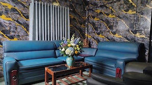A blue sofa, a coffee table, and a vase with flowers in a room with a marble-patterned wall.