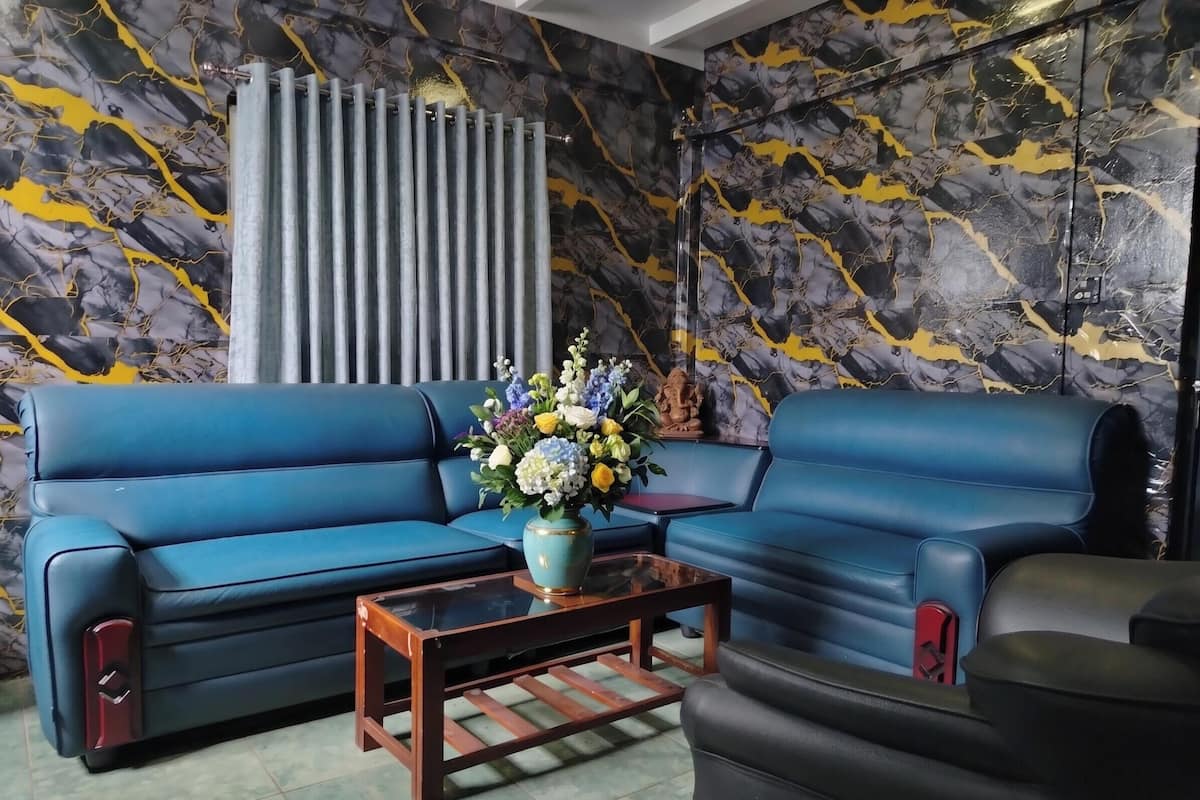 Un sofá azul, una mesa de centro y un florero con flores en una habitación con pared de diseño mármol.