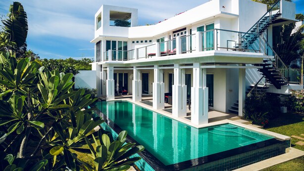 Una casa moderna de dos pisos con piscina, ventanas amplias y una escalera que lleva a un balcón.