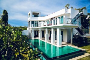 A modern two-story house with a swimming pool, large windows, and a staircase leading to a balcony.