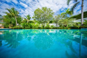 Une piscine d’eau cristalline, entourée d’une végétation luxuriante et de palmiers.