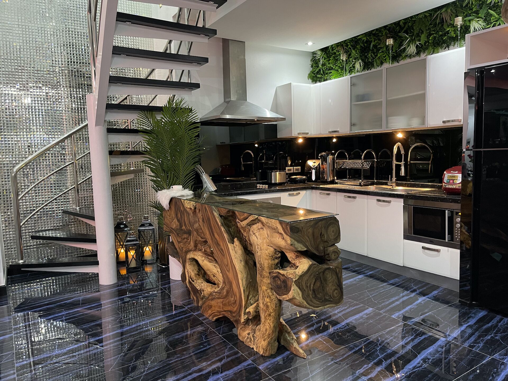 A modern kitchen with a central island, stainless steel appliances, and a staircase with glass railings.
