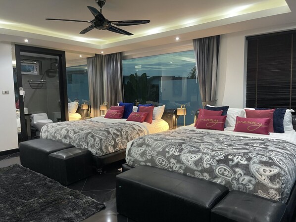 A modern hotel room with two beds, a ceiling fan, large windows, and a view of the outdoors.