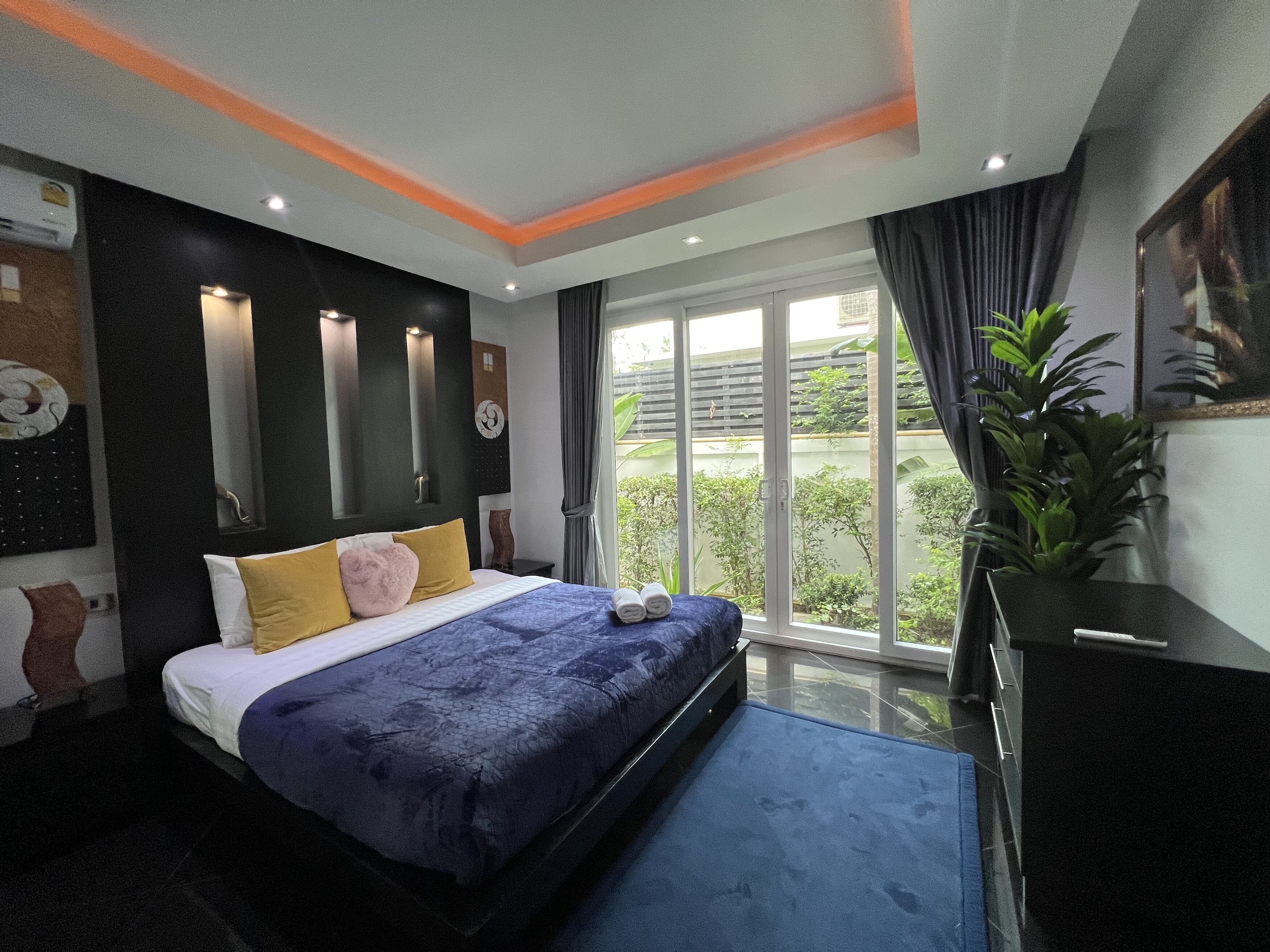 Une chambre moderne avec un grand lit, une porte-fenêtre coulissante donnant sur un balcon et une plante en pot.