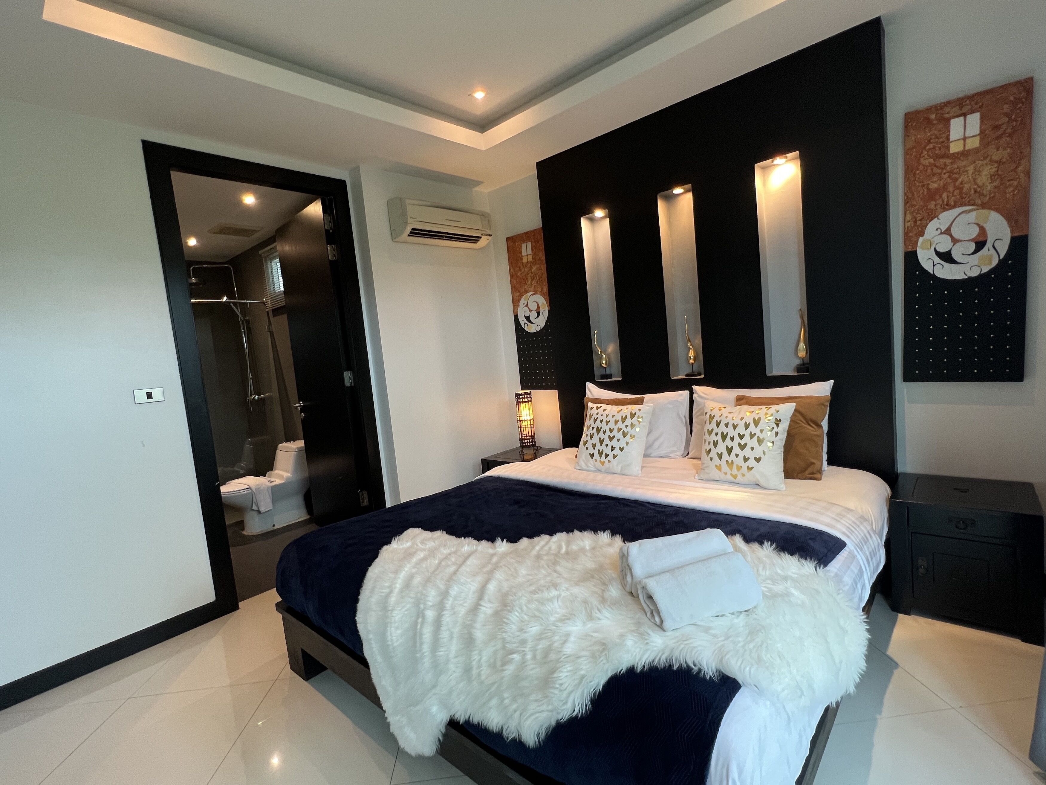 A modern hotel room with a large bed, a walk-in closet, and a bathroom with a glass shower enclosure.