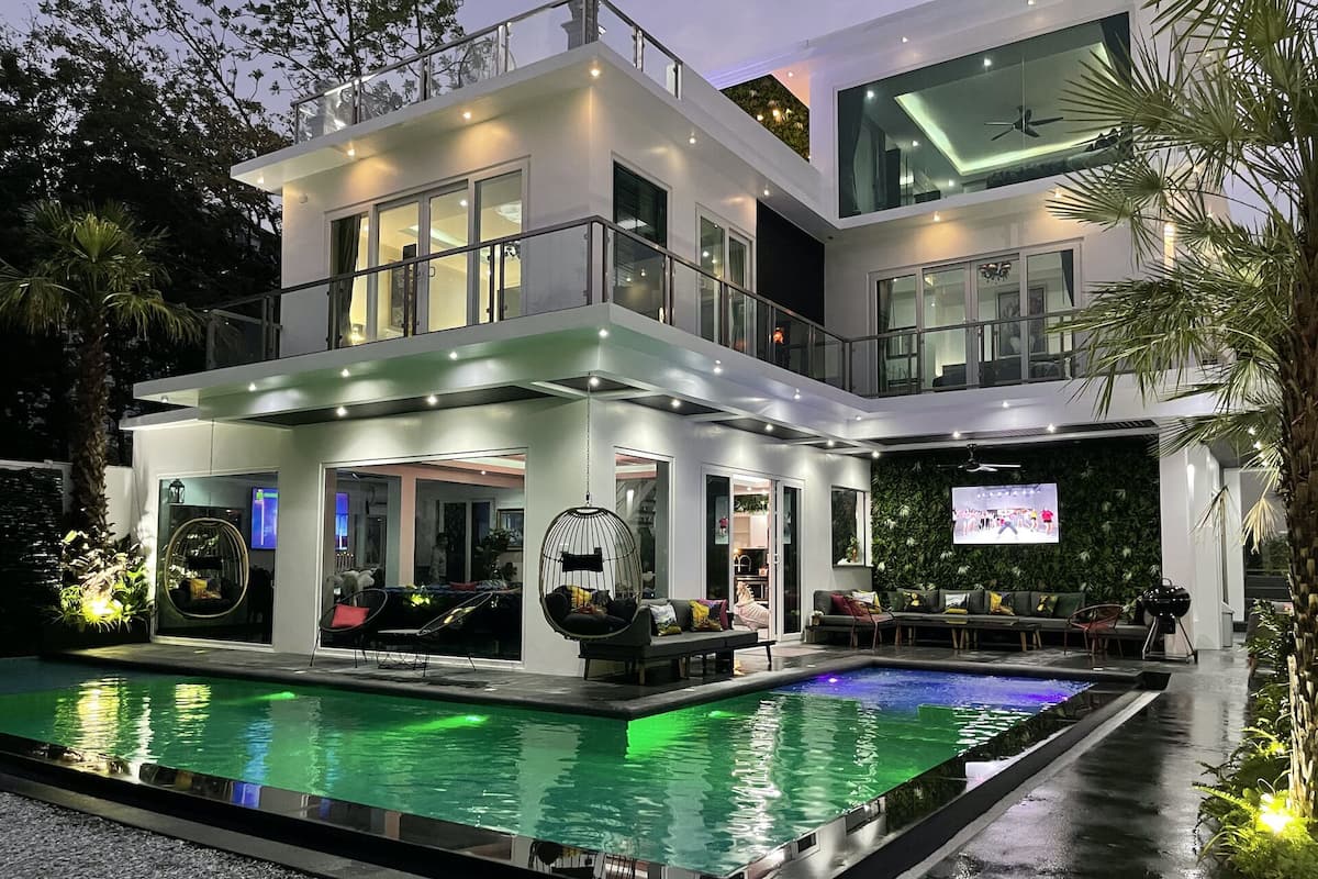 Ein modernes, zweistöckiges Haus mit Swimmingpool, Sitzgelegenheiten im Freien und einem großen Fernsehbildschirm.