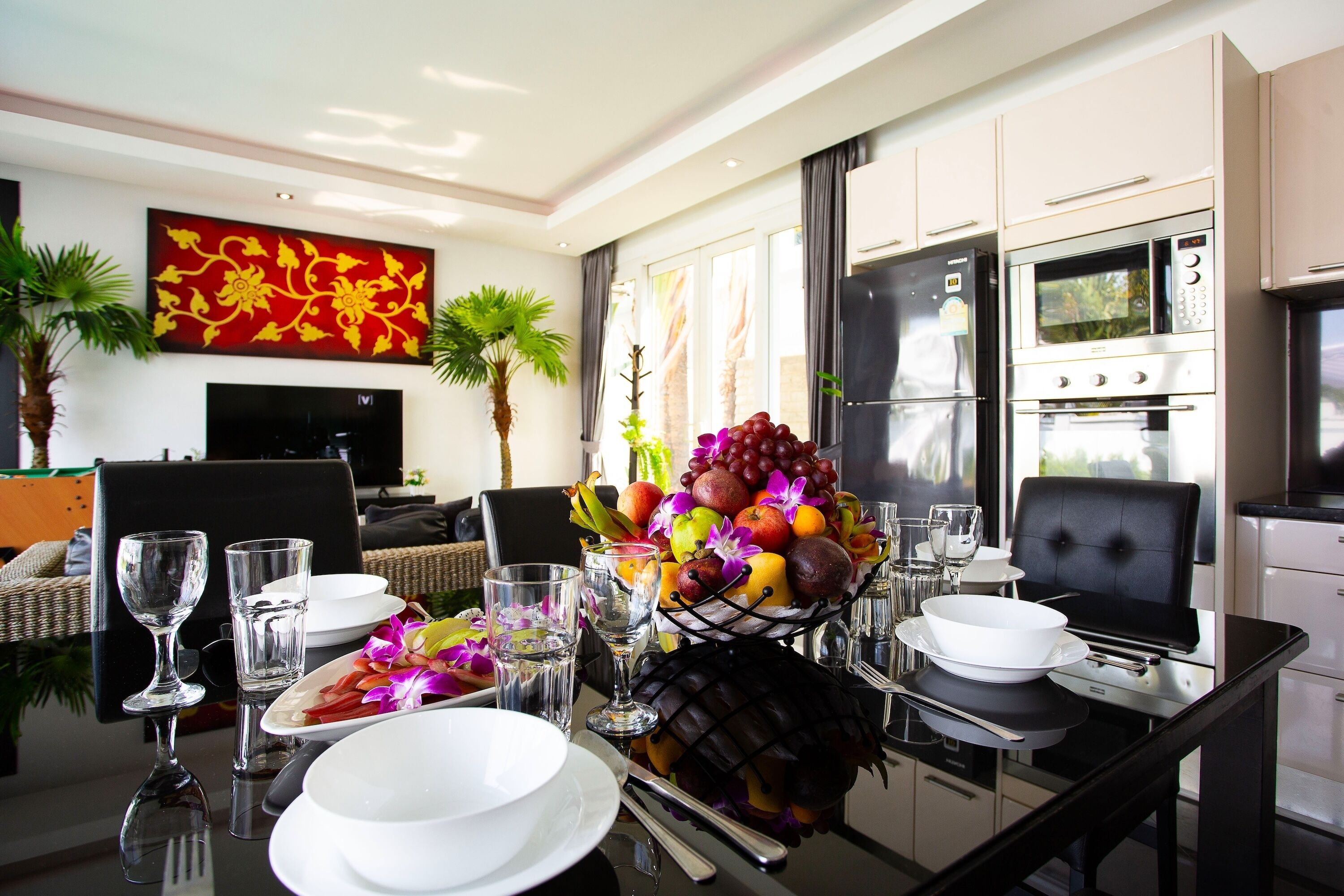A modern dining area with a glass table, white plates, and a fruit centerpiece.
