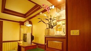 A compact room with wooden cabinetry, a small green cushioned bench, a yellow appliance, and a potted plant with flowers. - Highway Hotel (Chiang Mai)