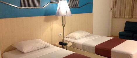 A hotel room with two beds, a nightstand with a lamp, a mirror, and a blue accent wall.