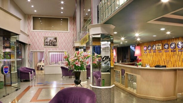 A hotel lobby with a reception desk, purple seating, and a decorative wall with clocks. - Highway Hotel (Chiang Mai)