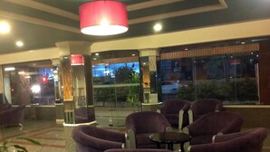 A lobby with purple chairs, a red hanging light, and a glass wall with a view of the outside. - Highway Hotel (Chiang Mai)