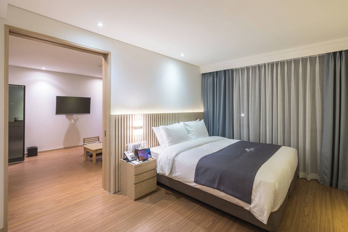Moderni hotellihuone, jossa on suuri sänky, yöpöytä ja seinälle asennettu taulutelevisio.