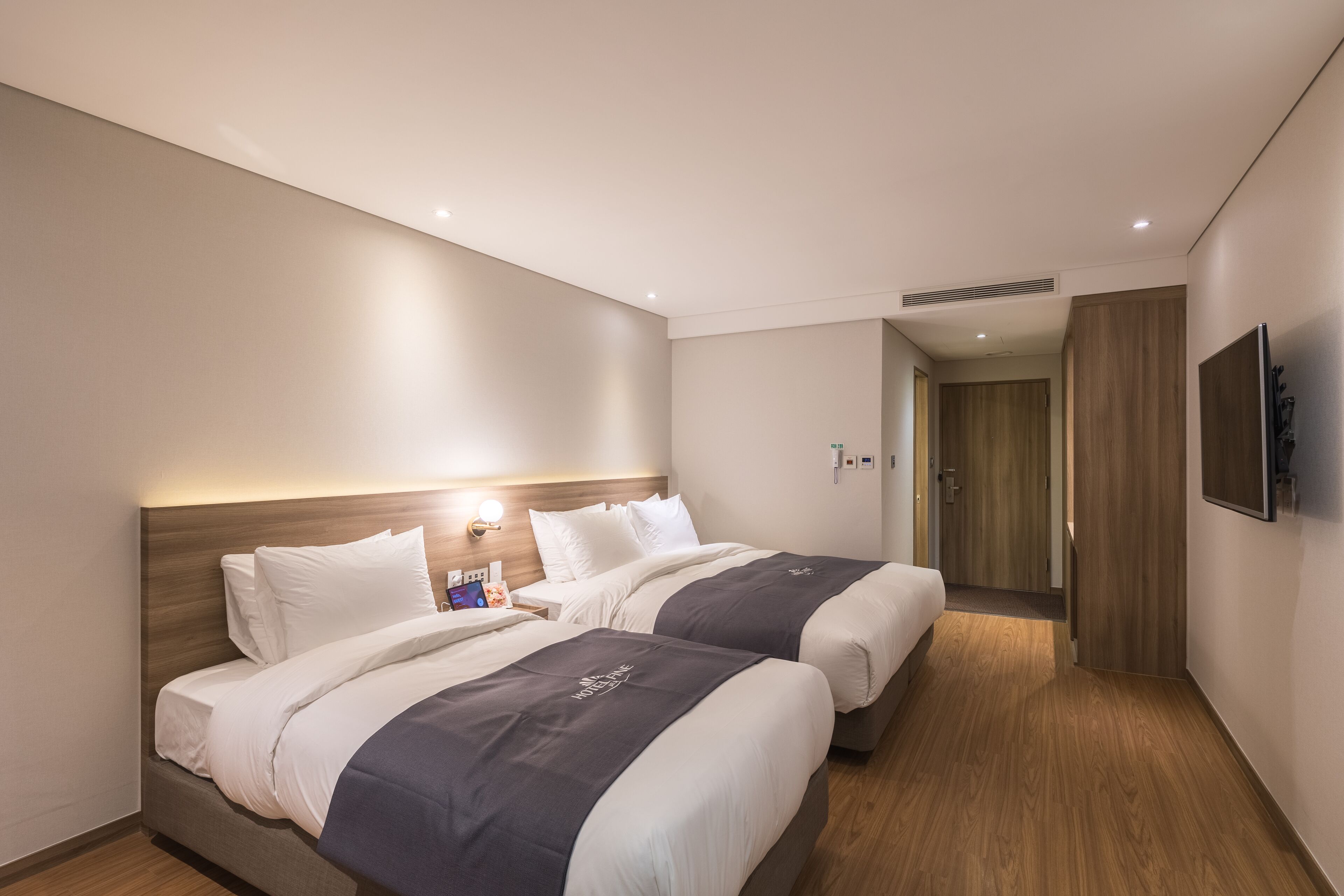 A hotel room with two beds, a TV mounted on the wall, and a wooden door in the background.