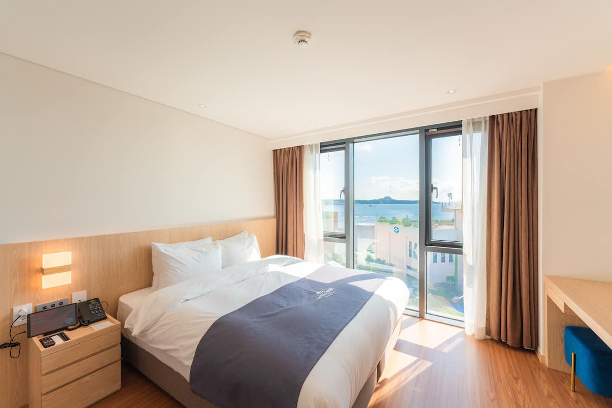 Hotellihuone, jossa on suuri sänky, työpöytä, taulutelevisio ja näkymä kaupunkiin.