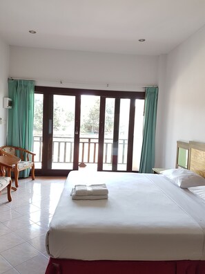 A hotel room with a bed, a chair, a table, and a view of the outside balcony.