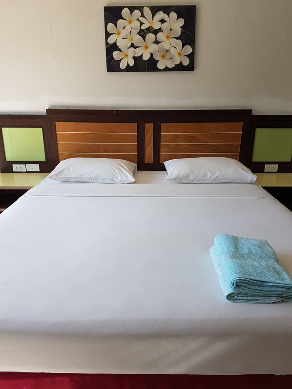 A neatly made bed with white linens, two pillows, and a folded blue towel.