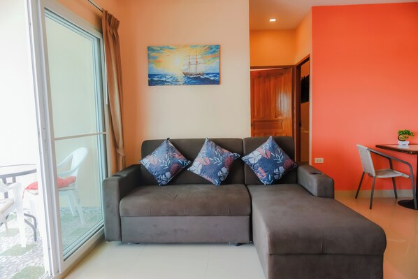 Uma sala de estar moderna com um sofá cinzento, três almofadas estampadas, um quadro de um navio na parede e uma área de jantar com mesa e cadeiras.