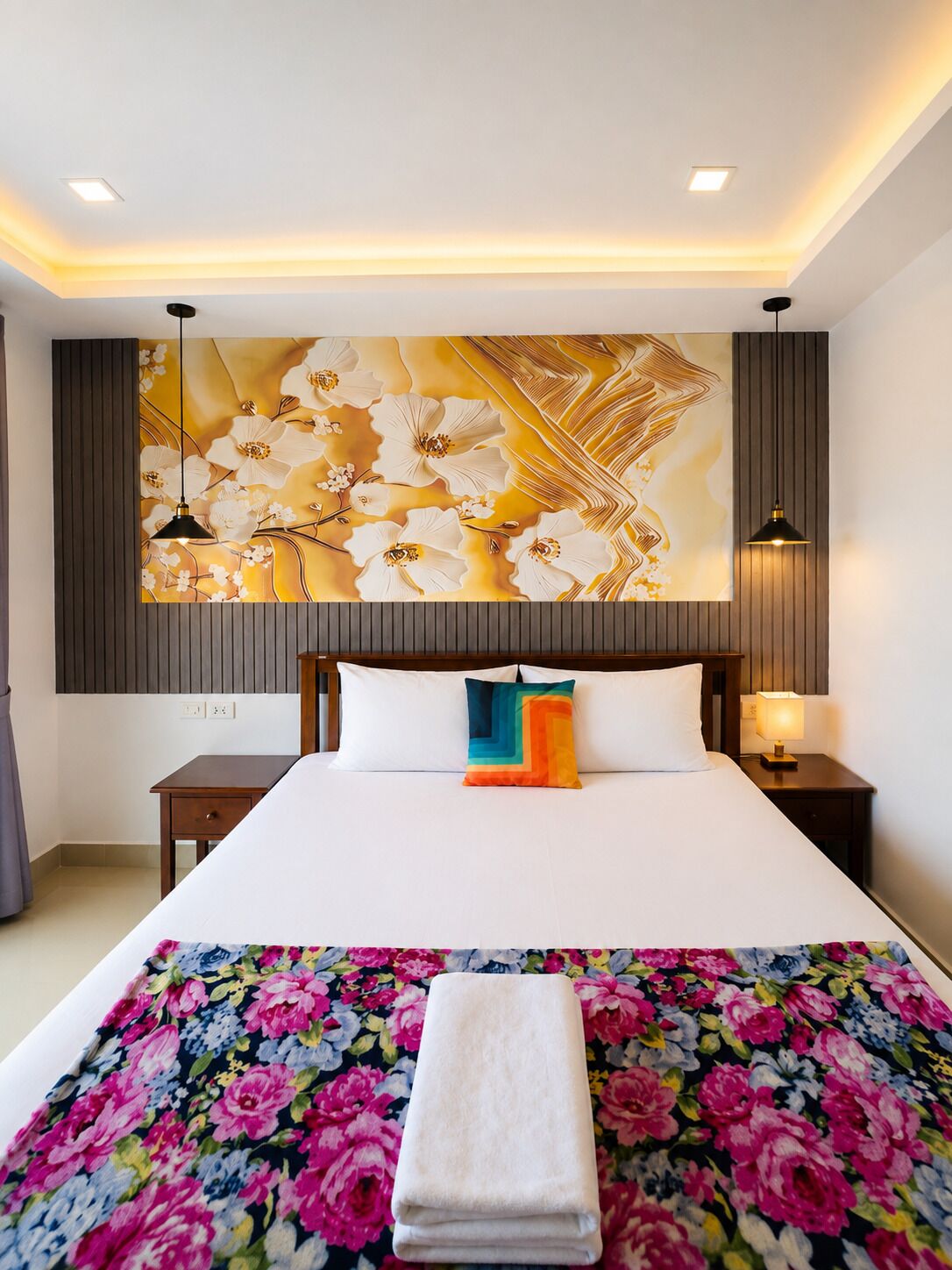 Une chambre d’hôtel avec un grand lit, une œuvre d’art accrochée au mur, une table de chevet avec une lampe et une serviette pliée posée sur le lit.