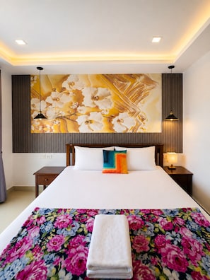 Habitación de hotel con una cama grande, una obra de arte colgada en la pared, una mesita de noche con lámpara y una toalla doblada sobre la cama.