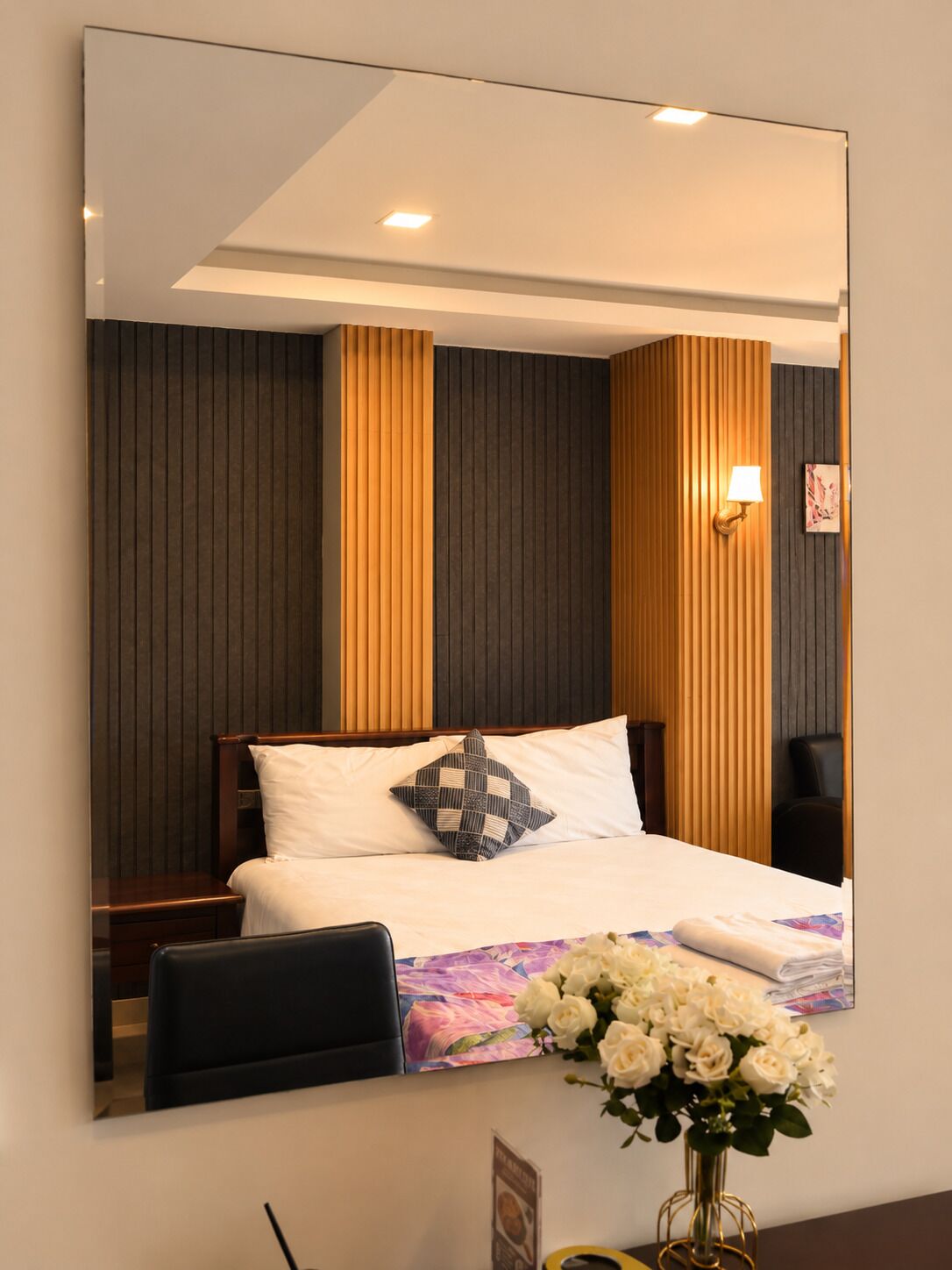 Ein Hotelzimmer mit einem großen Bett, einem Nachttisch, einem Sessel, einer Wandlampe und einem Spiegel, der den Raum wiedergibt.