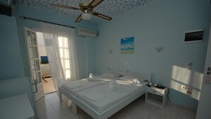 A bedroom with two beds, a ceiling fan, an air conditioning unit, a small table, and a window with curtains. - Ocean View (Naxos)