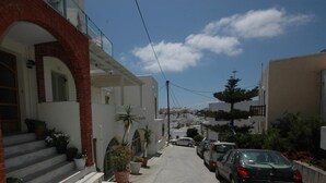 A narrow street with parked cars and a building with a red brick archway. - Ocean View (Naxos)