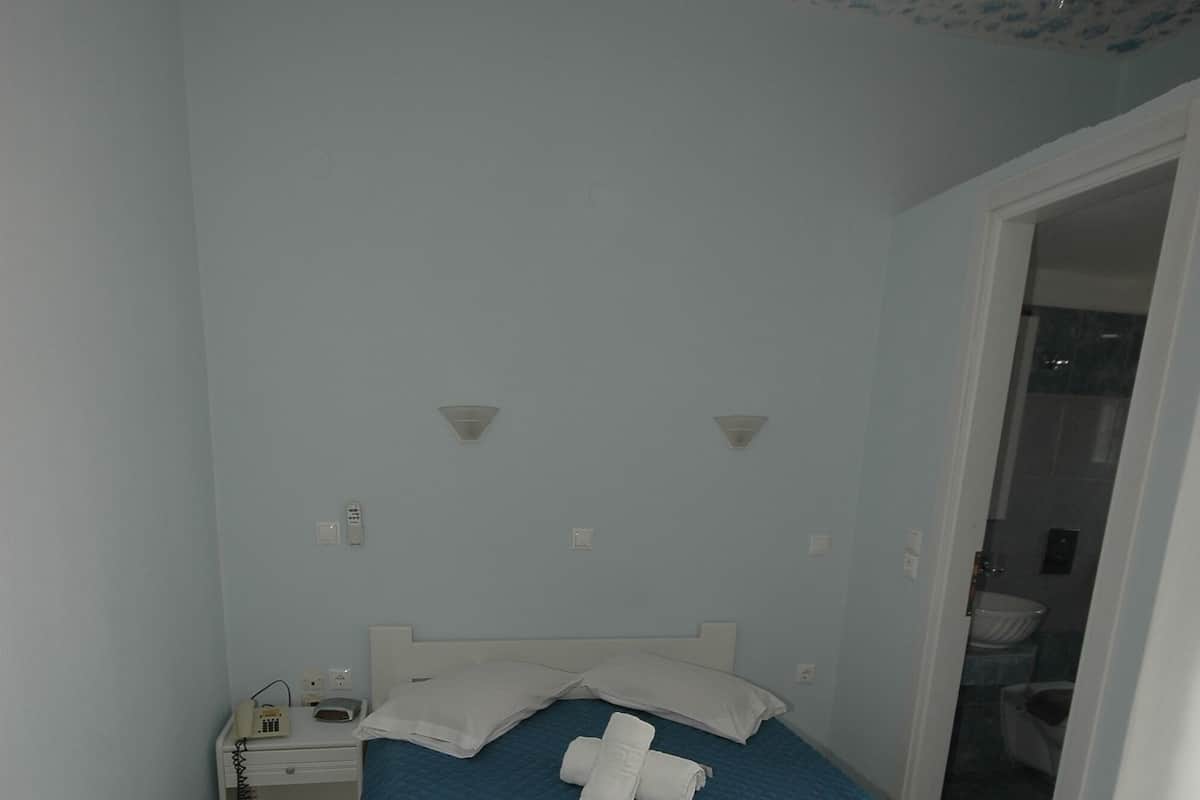 A bedroom with a bed, a nightstand, a ceiling fan, and a bathroom visible through an open door.