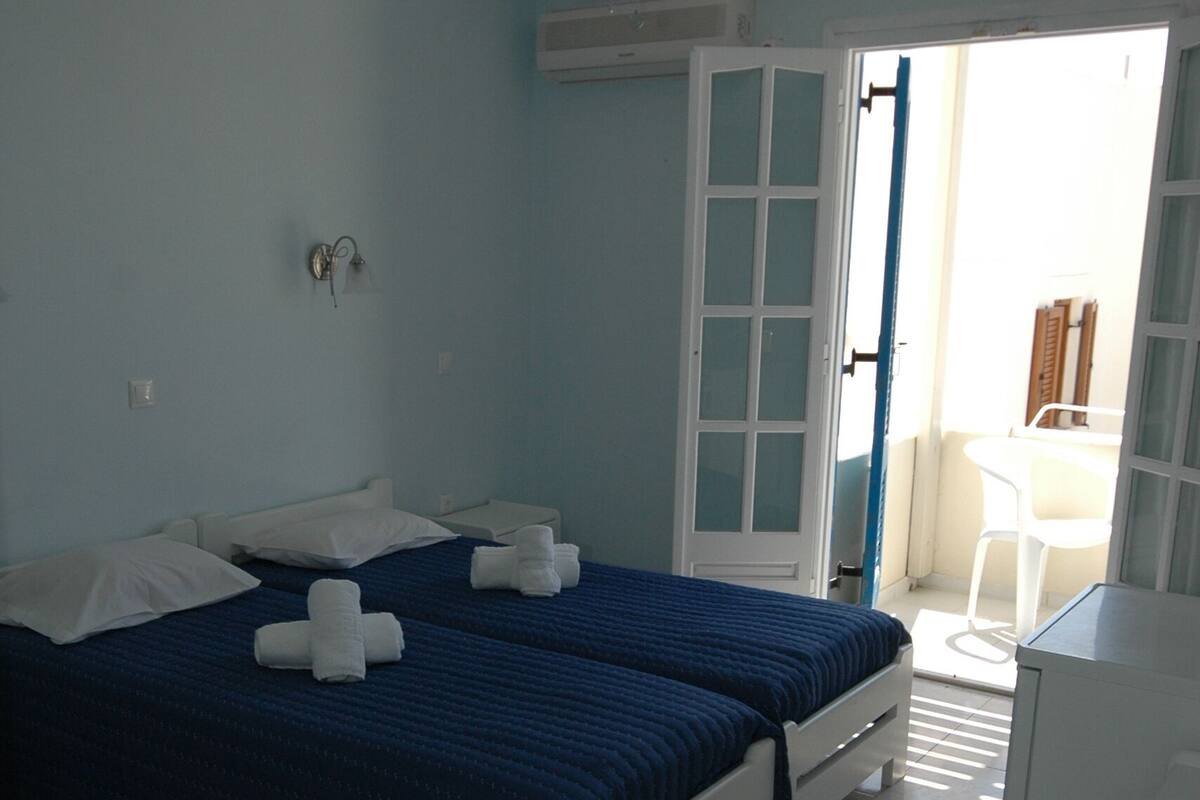 A bedroom with two beds, a ceiling fan, and a view of the outside through an open door.