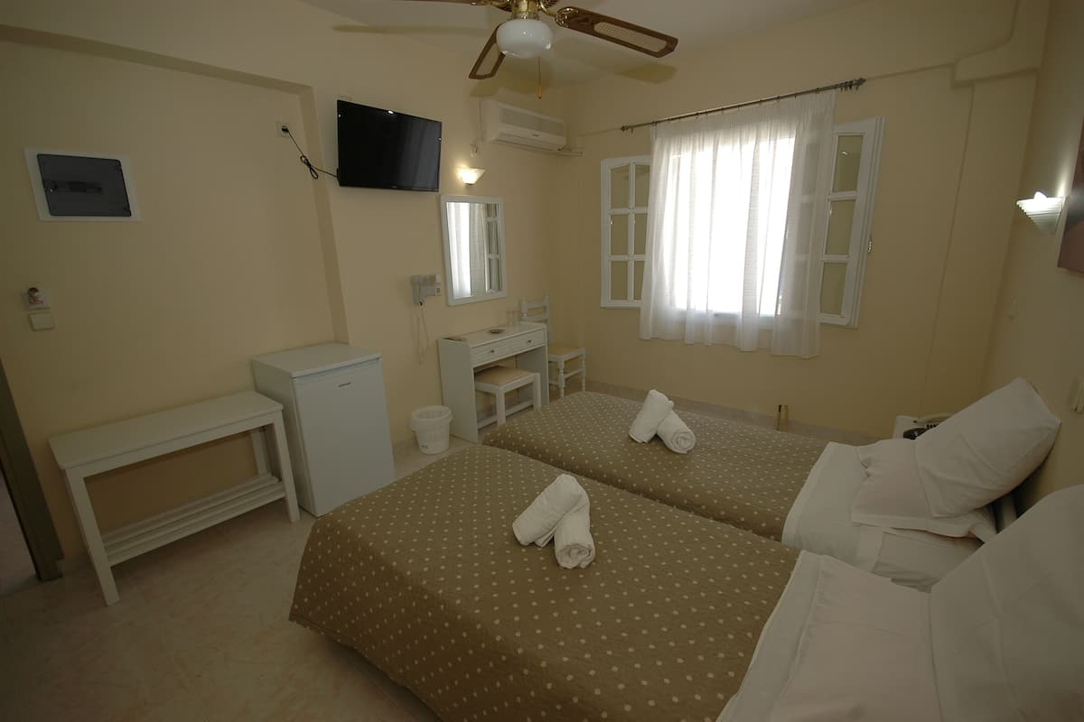 A hotel room with two beds, a desk, a chair, a small table, a TV, and a window with curtains.