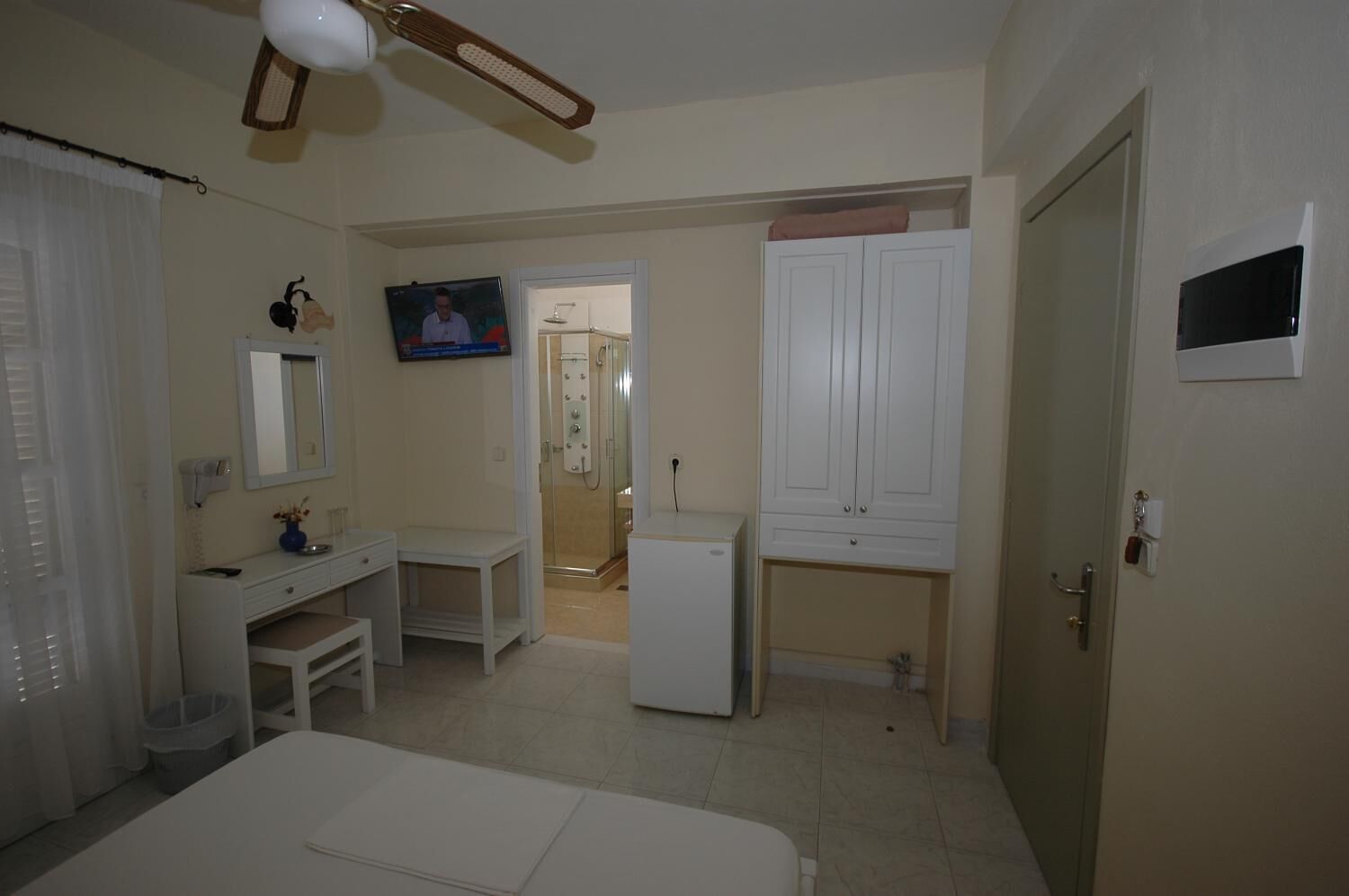 A bedroom with a bed, a vanity with a mirror, a television, a wardrobe, and a shower area.
