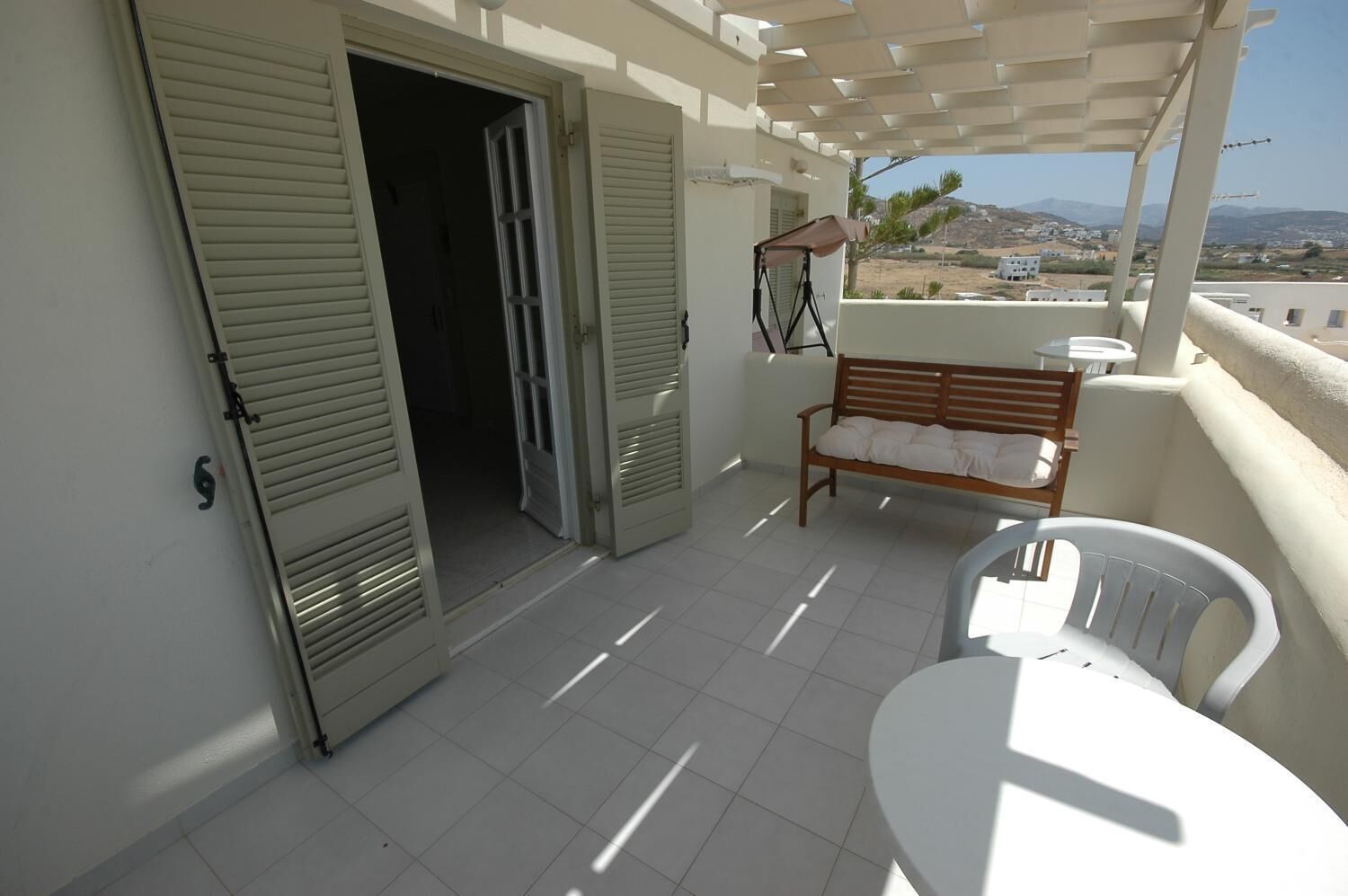A balcony with a wooden bench and a table, a door, and a view of the landscape.