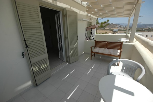 Ein Balkon mit einer hölzernen Bank und einem Tisch, einer Tür und Blick auf die Landschaft.