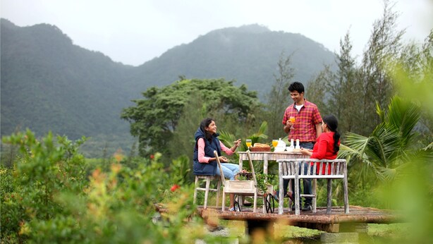 A wooden deck with a table and chairs overlooking a lush garden and mountains. - Harvest Fresh Farms (Uthamapalayam)