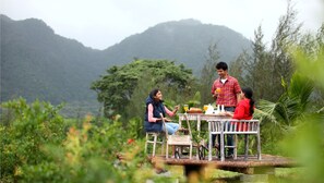 A wooden deck with a table and chairs overlooking a lush garden and mountains.
