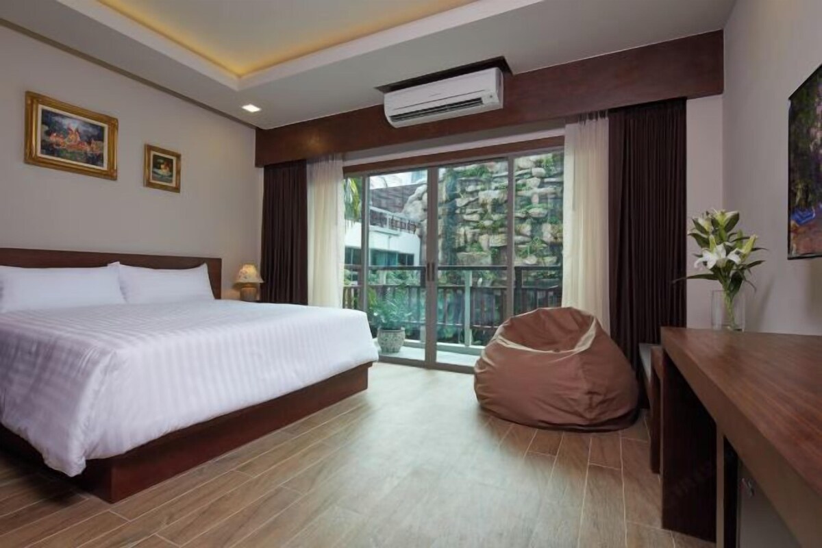 A hotel room with a bed, a bean bag chair, a desk, and a large window with a view.