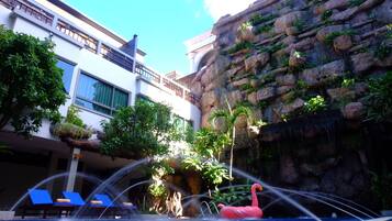 Relax by the pool surrounded by lush greenery and a rock wall, with a central water feature and lounge chairs nearby.
