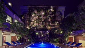 Une piscine avec des chaises longues, un mur d’escalade agrémenté de verdure et un bâtiment doté de balcons.