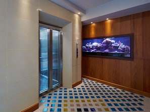 A modern elevator with glass doors, a patterned floor, and a wall-mounted aquarium. - The AGATE Pattaya Boutique Resort (Pattaya)