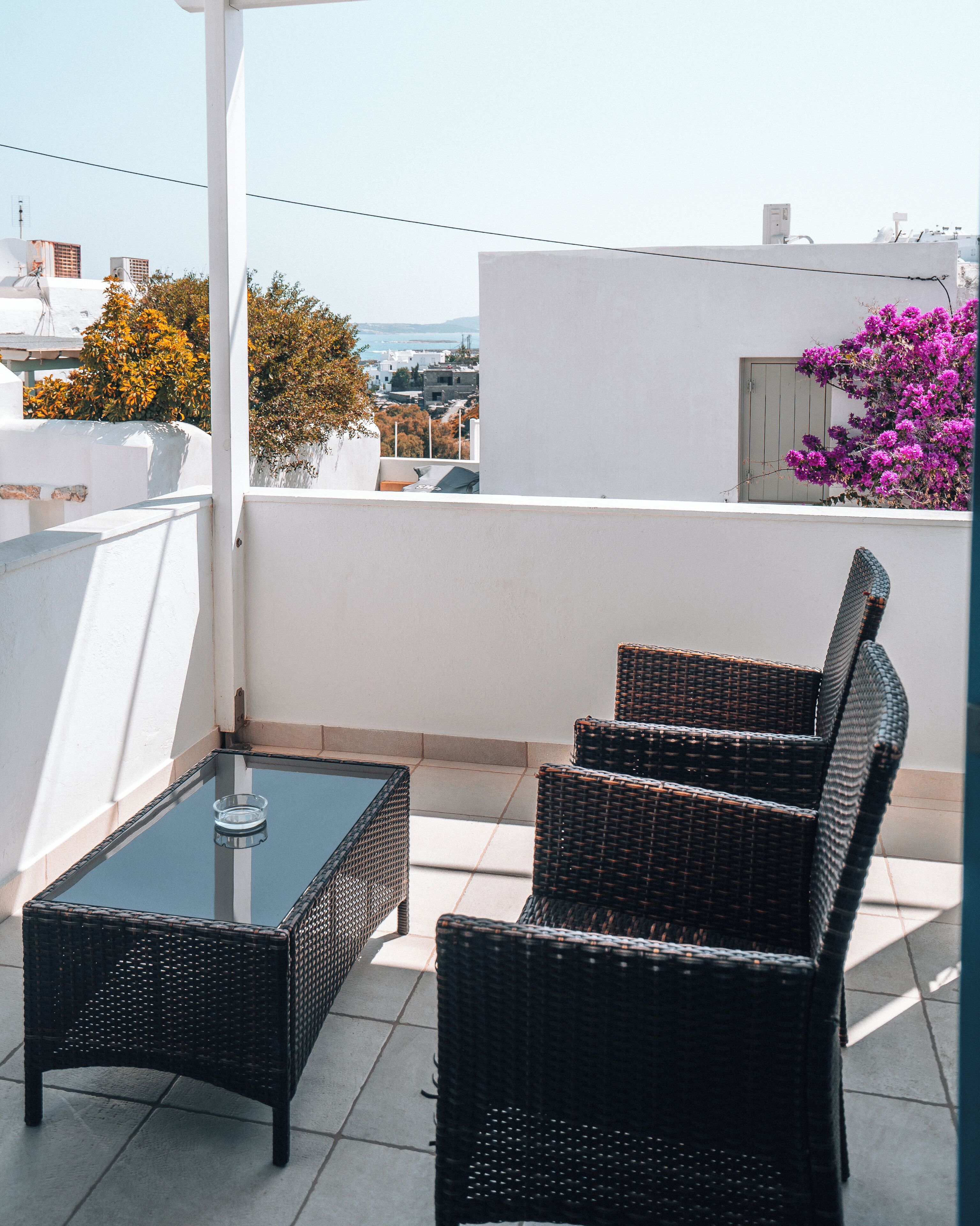 A balcony with wicker furniture, a glass table, and a view of the cityscape.