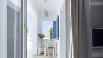 A room with a sliding glass door leading to a balcony with a stone floor, a white table with chairs, and a potted plant.