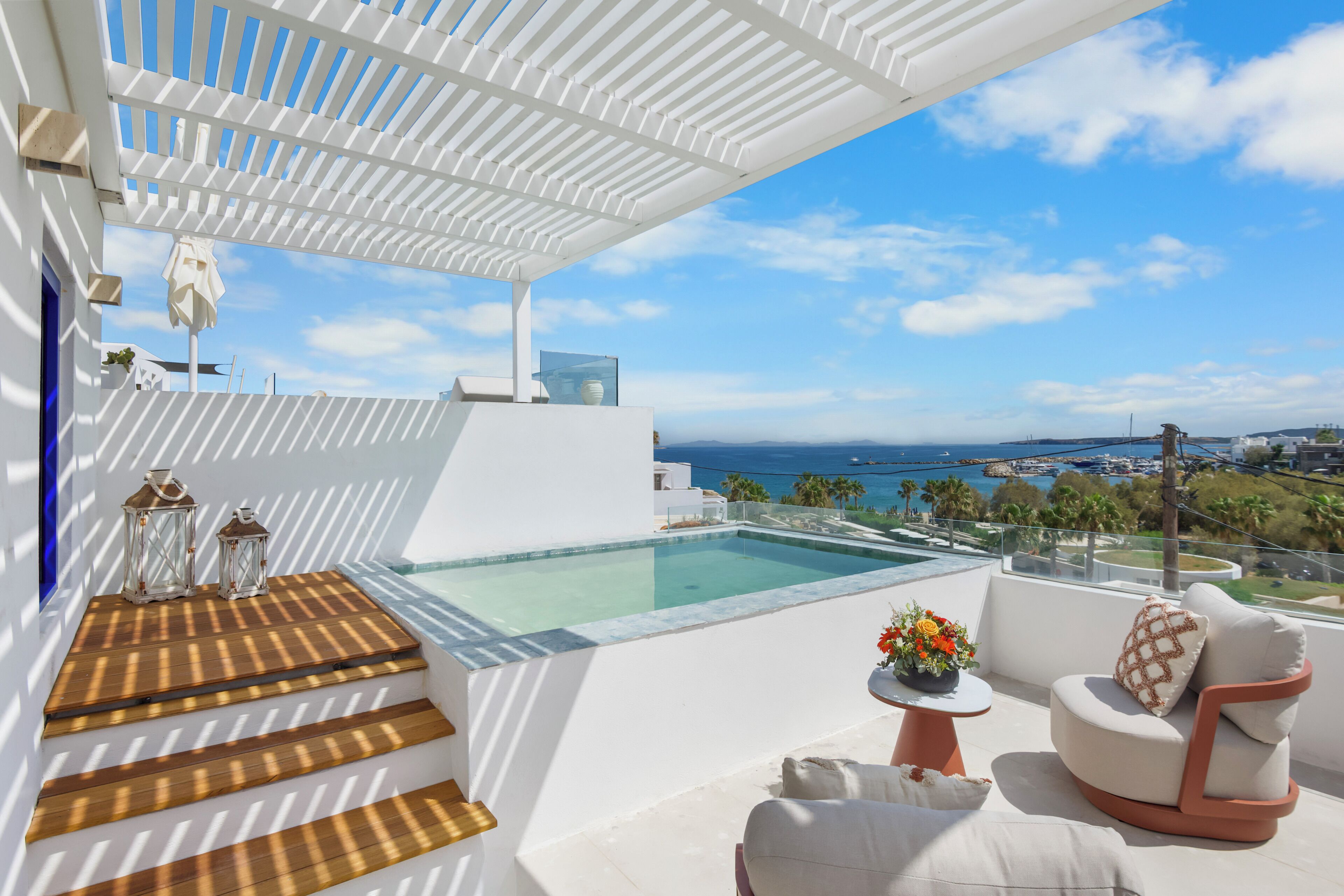 Una terraza moderna al aire libre con piscina, mobiliario blanco y vistas despejadas al mar.