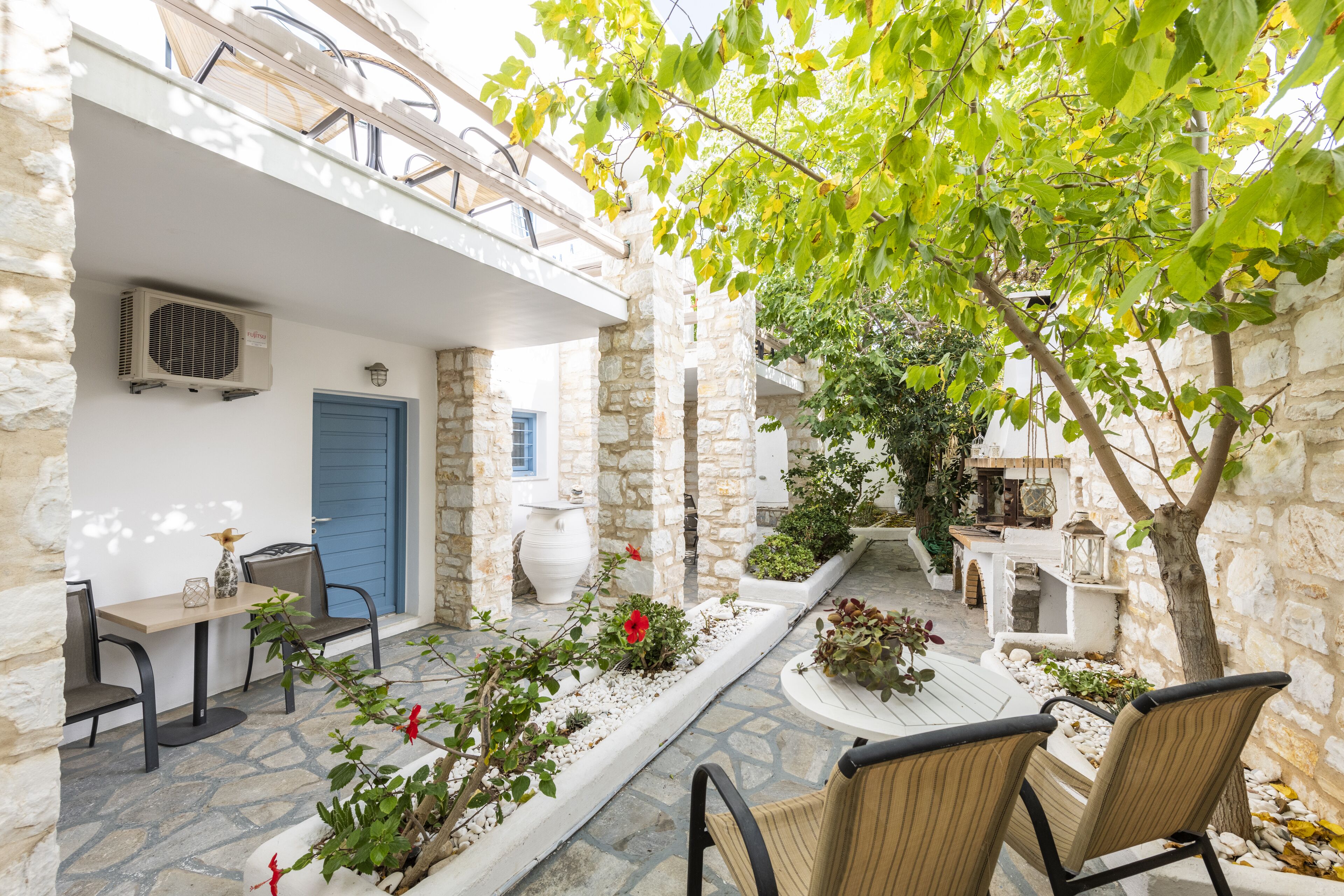 A courtyard with stone walls, a blue door, outdoor seating, and potted plants.