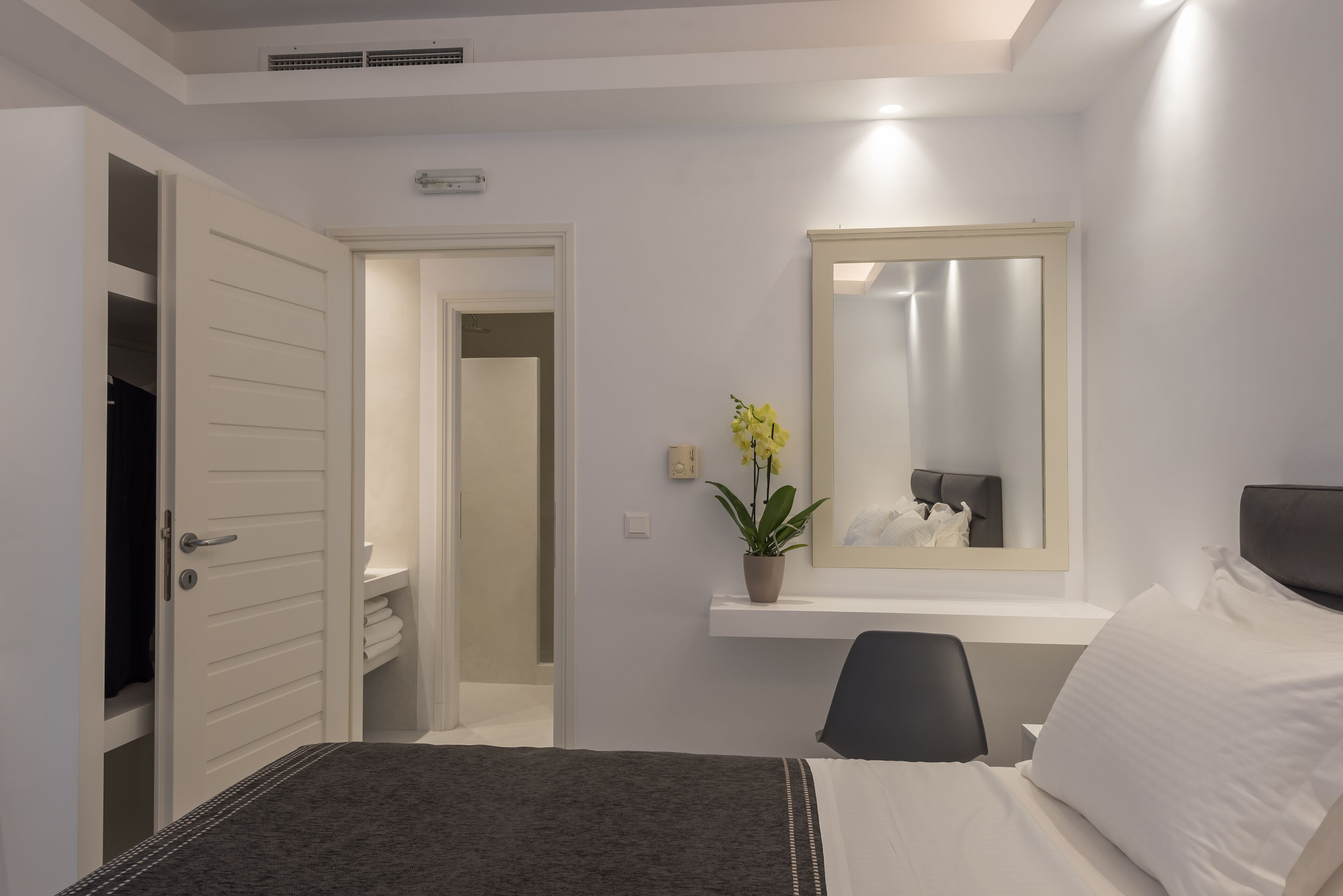 Quarto de hotel com cama, escrivaninha, cadeira, espelho e planta em vaso.