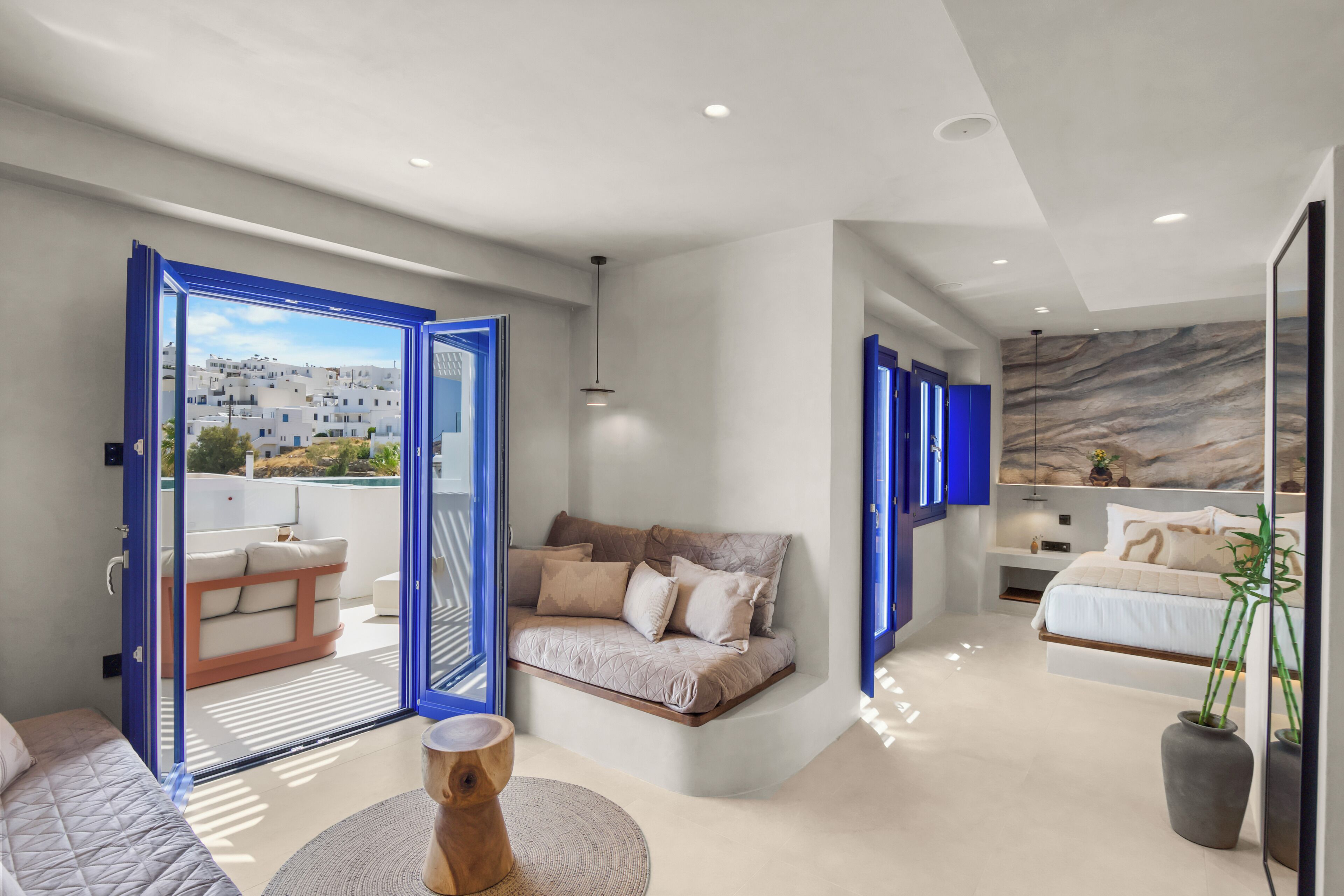 A modern interior with a sofa, a round wooden table, and a view through an open door to a balcony.