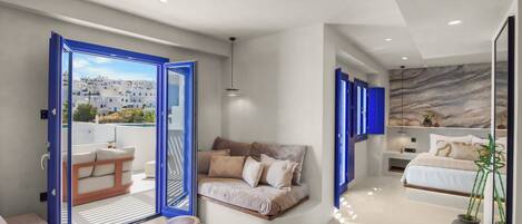 A modern interior with a sofa, a round wooden table, and a view through an open door to a balcony.