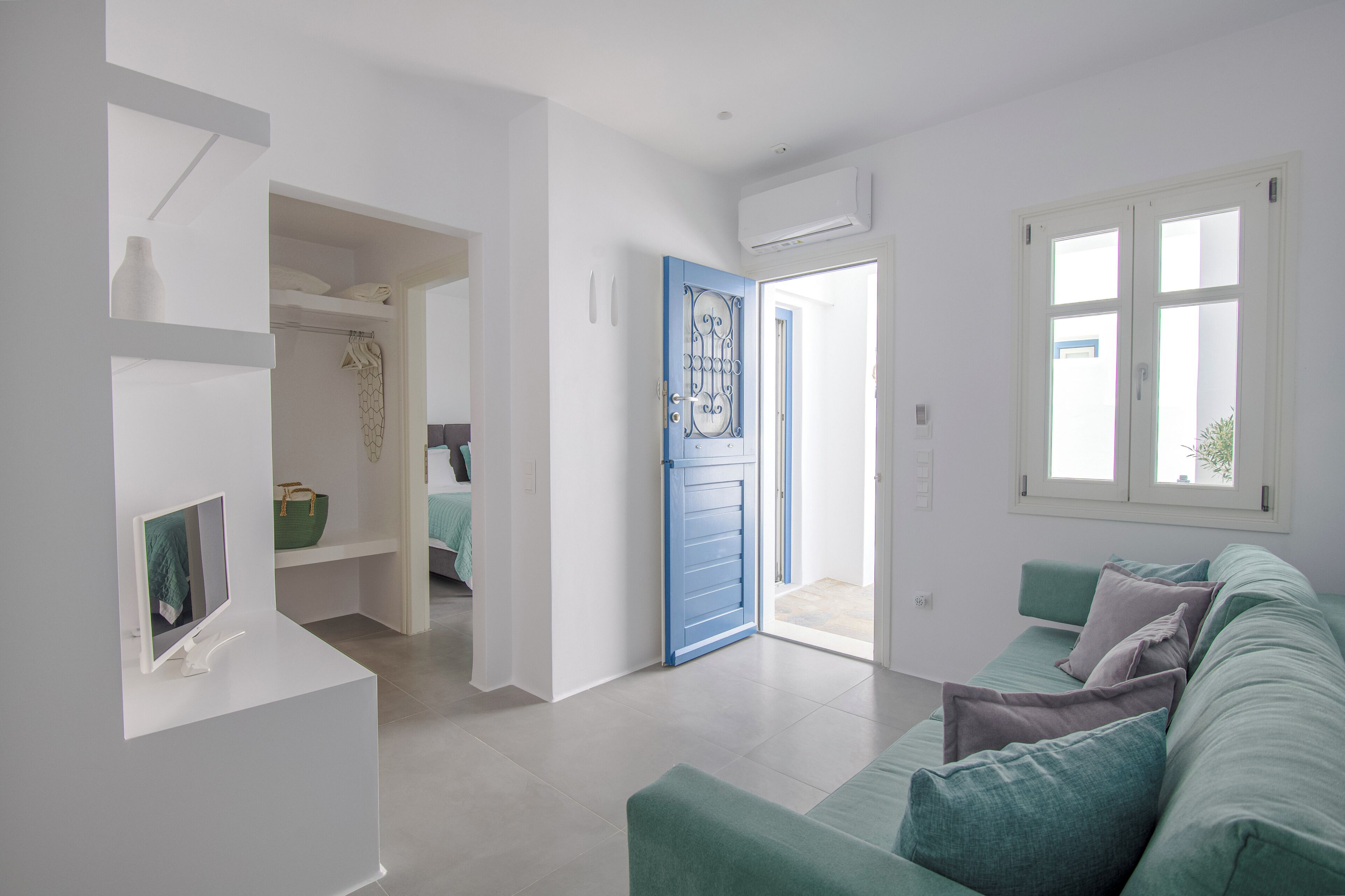 A modern living room with a teal sofa, a white console table, and a blue door leading to a bathroom.