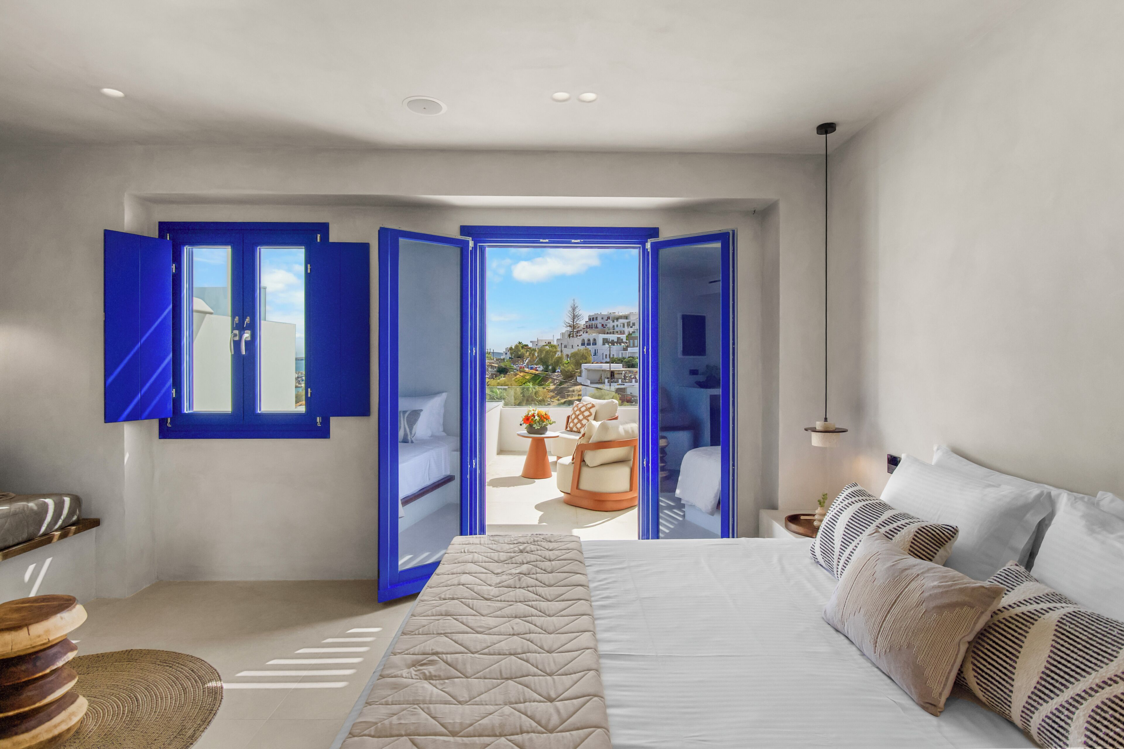 Un dormitorio con cama, vista a la ciudad y balcón con mobiliario exterior.