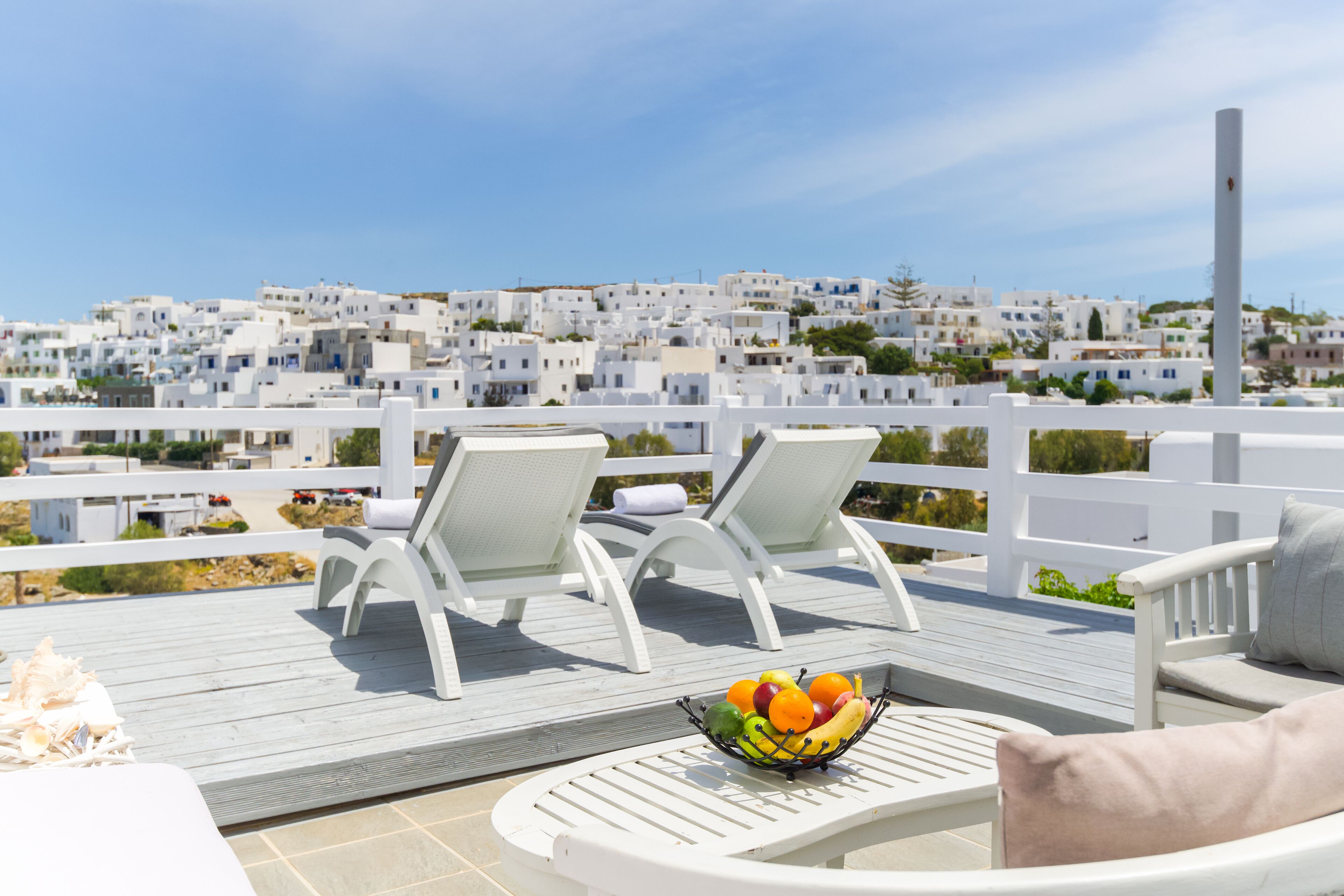 A balcony with white furniture, a fruit bowl, and a view of white buildings.